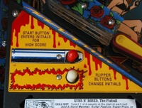 Image # 33086: Guns N' Roses Sample Game - Left Apron Sticker 
(On production games, the words 'Shoot Again' are printed to the left of the red bulb, and 'Magnets On' to the left of the white bulb. Game has serial number 110878 manufactured May 23, 1994.)